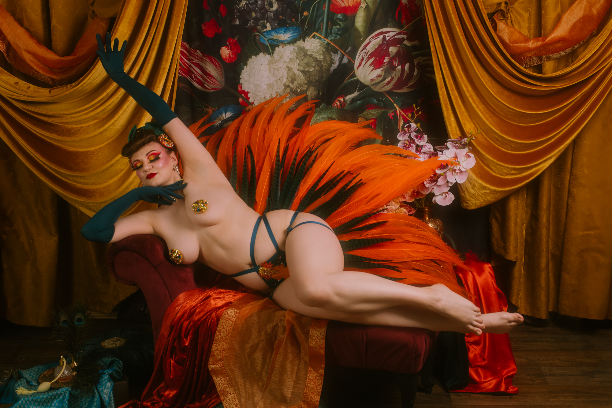 Kobieta o pięknych kształtach wyciąga się leniwie na szezlongu. Wokół niej jest scenografia w pomarańczowym i turkusowym kolorze.