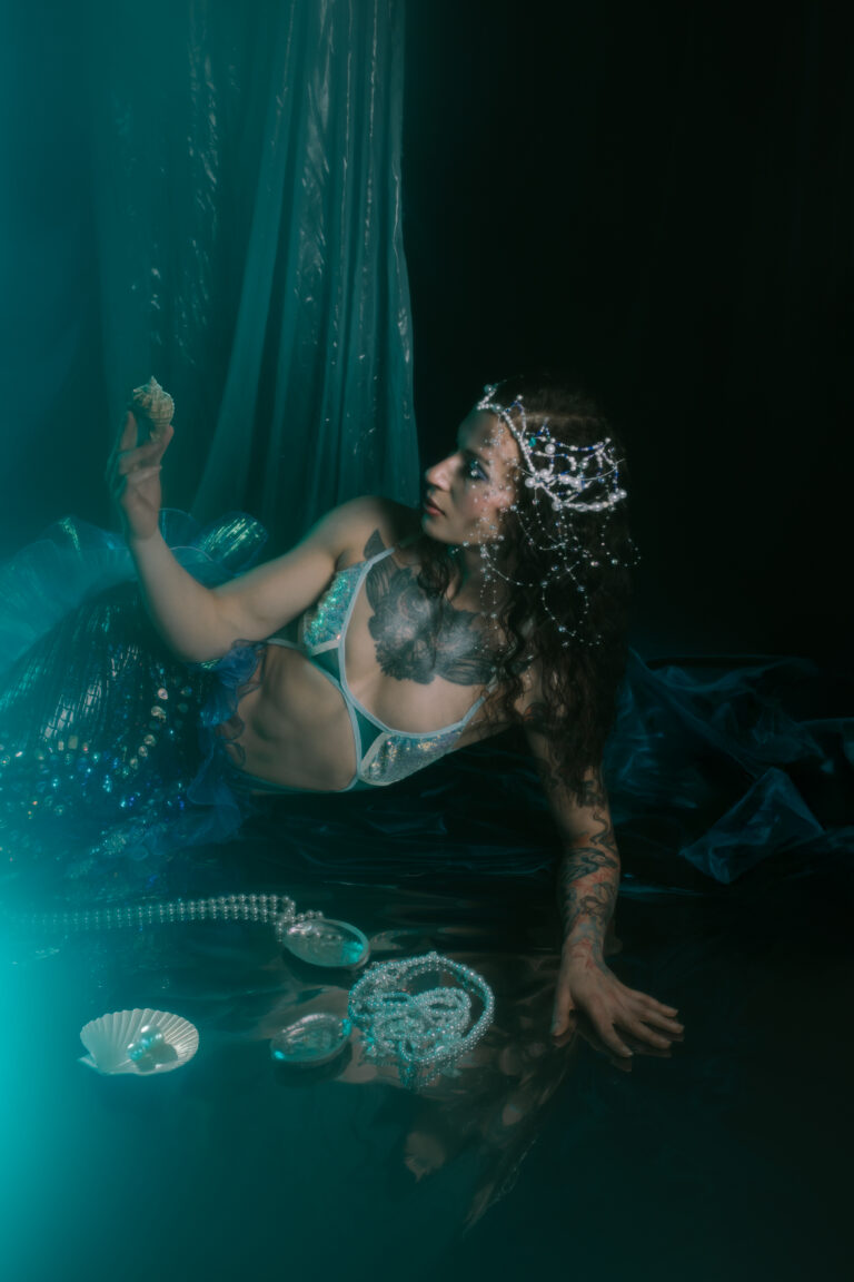 Kobieta w syrenim ogonie trzyma w dłoni muszlę.