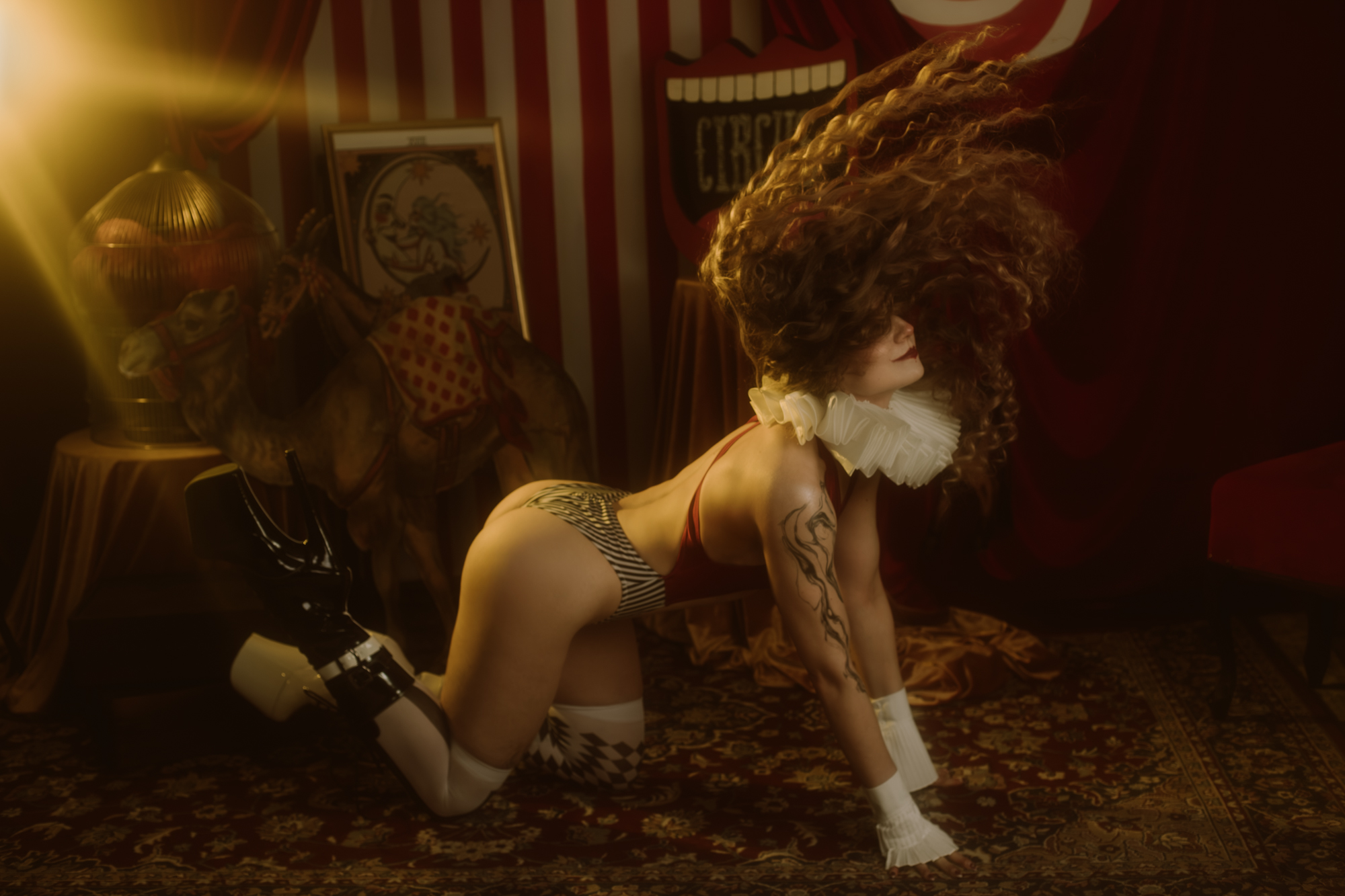 Kobieta z długimi kręconymi włosami odrzuca je fantazyjnie do tyłu klęcząc.