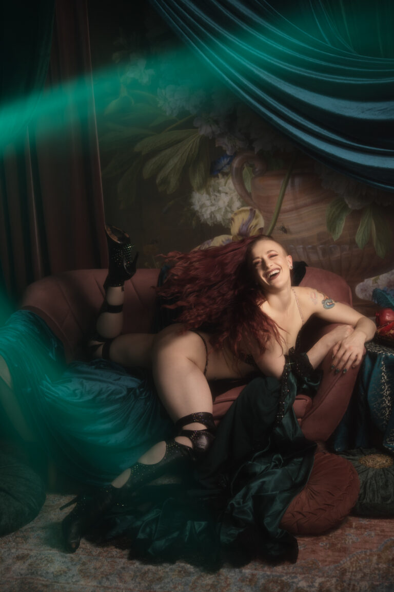 Kobieta radośnie podrzuca rudymi włosami leżąc na sofie w fantazyjnej pozie.