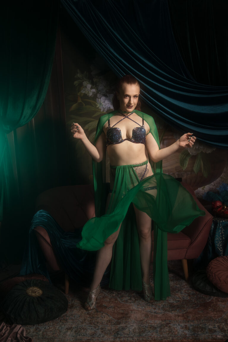 Kobieta w błyszczącej bieliźnie podrzuca panelową spódnicę z zielonego tiulu.