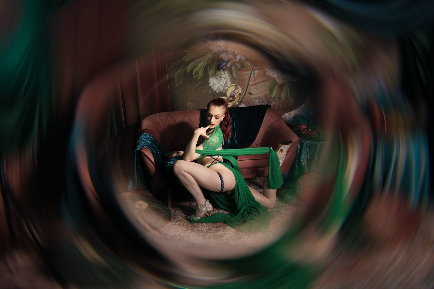 Rudowłosa kobieta w zielonym szlafroku kuca na tle scenografii.